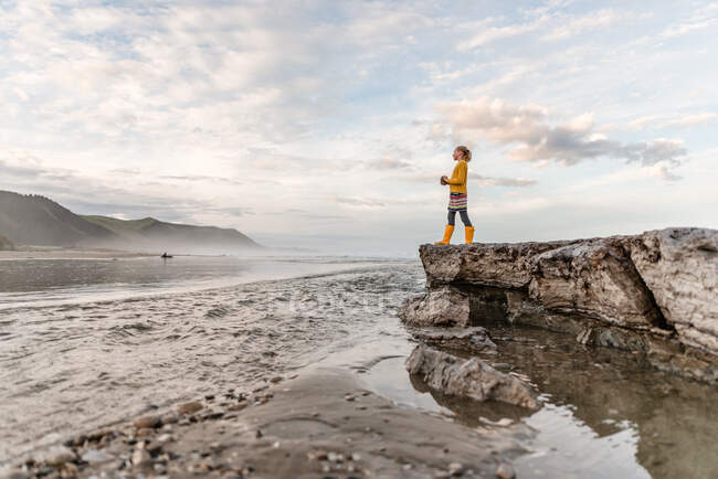 Menina pré-adolescente em pé sobre pedras na praia na Nova Zelândia — Fotografia de Stock