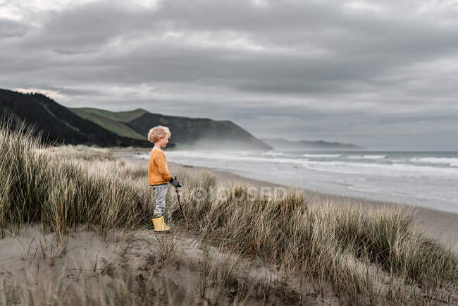Loira encaracolado menino assistindo o oceano em um dia nublado na Nova Zelândia — Fotografia de Stock
