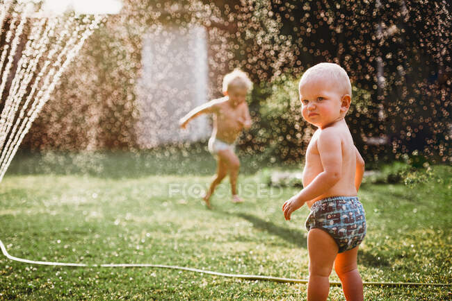 Bambini piccoli che giocano con l'acqua dell'irrigatore nel cortile — Foto stock