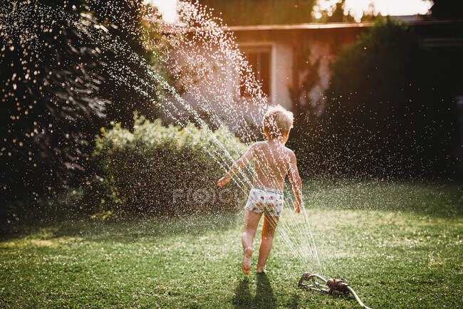 Menino feliz jogando e salpicando água no quintal. — Fotografia de Stock