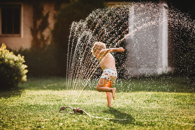 Щасливий хлопчик грає і бризкає воду на задньому дворі . — стокове фото