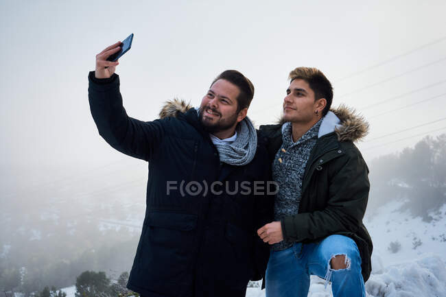 Два парня позируют и фотографируют со своим телефоном в окружении снега — стоковое фото