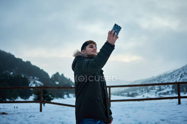 A young man takes a selfie with his mobile phone on a snowy day — Stock Photo