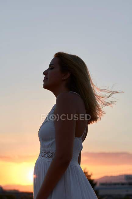 Jeune femme ferme les yeux tandis que le vent caresse son visage au coucher du soleil — Photo de stock