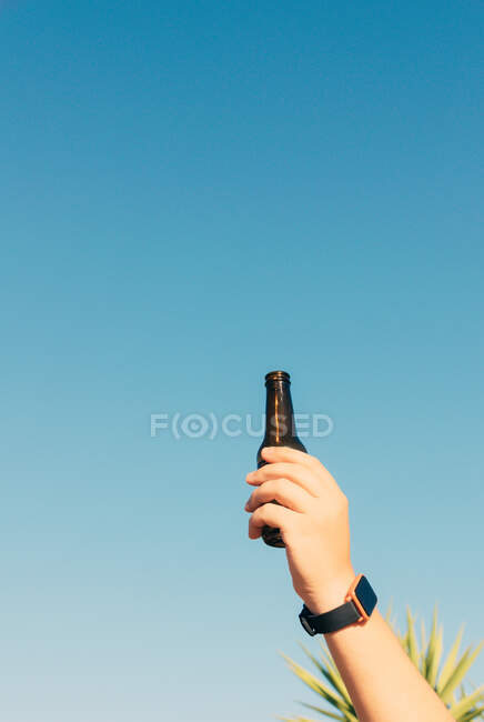 Vertical shot of bottle lifted high on blue sky background — Stock Photo