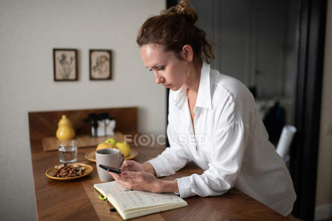 Взрослая деловая женщина проверяет уведомления на смартфоне, работая дома — стоковое фото