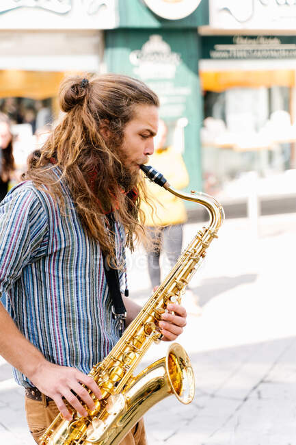 Vertical photo of the portrait of a young man with long hair playing saxophone in the street — Stock Photo