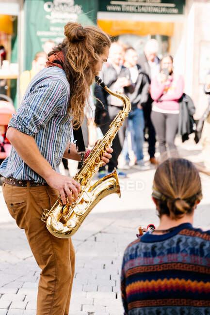Foto vertical de un saxofonista en su espalda tocando el saxofón junto a un guitarrista en la calle - foto de stock