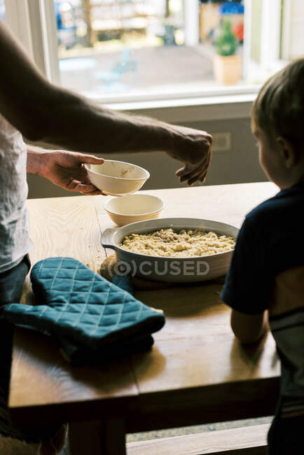 A father and son putting streusel on a peach cobbler — Stock Photo