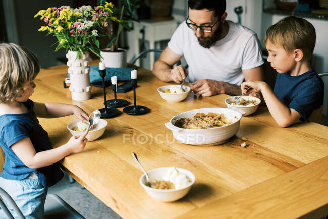 Una familia disfrutando de su zapatero de melocotón casero en la mesa de la cocina - foto de stock