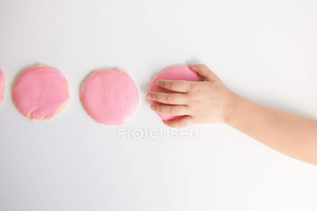 Overhead view of child's hand taking pink frosted sugar cookie — Stock Photo
