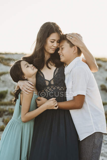 Schöne dunkelhaarige Mutter umarmt ihre kleine Tochter und ihren Sohn — Stockfoto