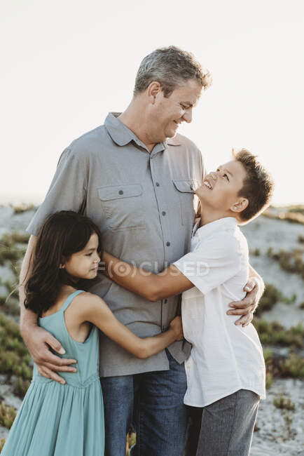Тато середини-40 у сірій сорочці обіймає дев'ятнадцятьох сина та молоду доньку — стокове фото