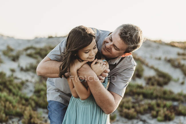 Sorrindo pai meados dos anos 40 abraçando a jovem filha perto de duna de areia — Fotografia de Stock