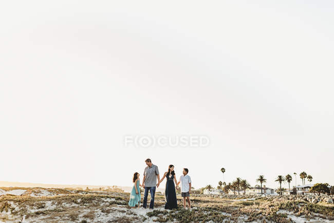 Щаслива сім'я тримає руки, стоячи на пляжі — стокове фото