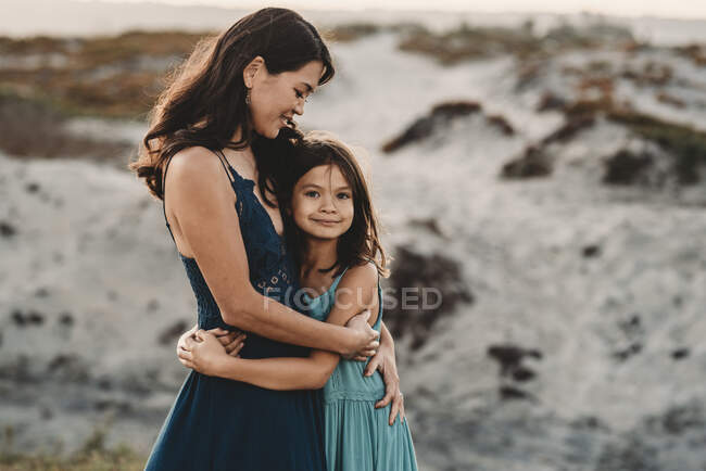 Beautiful 45 yr old mom embracing young daughter at the beach — Stock Photo