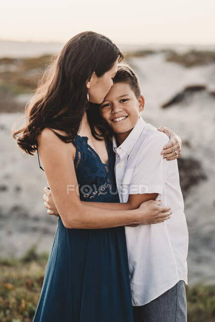 Beautiful mom tenderly embracing handsome preteen son at the beach — Stock Photo