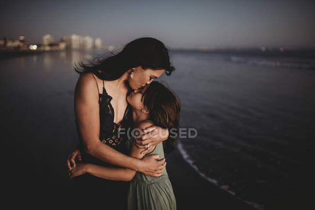 Mère tendre embrassant et embrassant 8 ans fille sur la plage au coucher du soleil — Photo de stock
