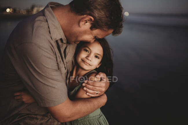 Mid-40's dad hugging 8 yr old daughter on beach at sunset — Stock Photo