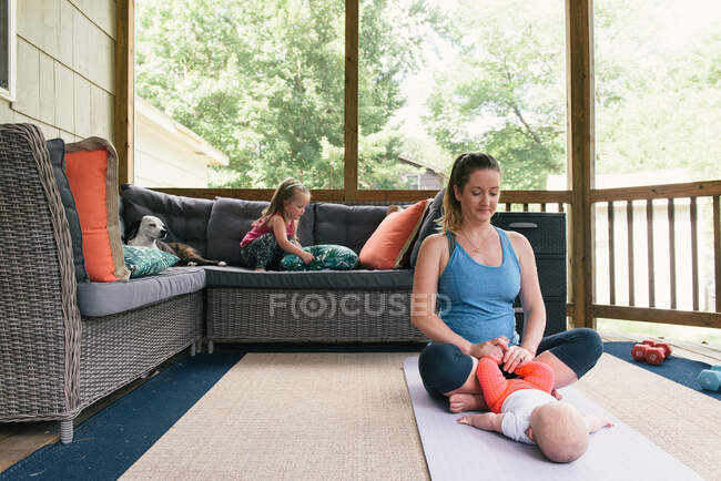 Heureuse jeune mère faisant des exercices de yoga sur la terrasse à la maison — Photo de stock