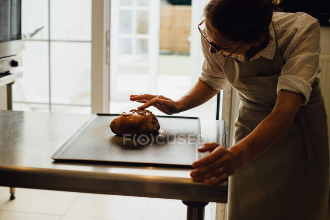 Female baker in uniform is decorating bread while working in bakery — Stock Photo