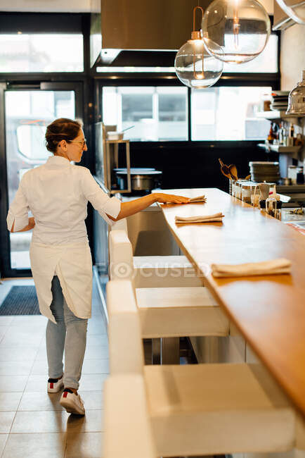Chef femenino poniendo servilletas en el mostrador de bar en el restaurante de cocina abierta - foto de stock