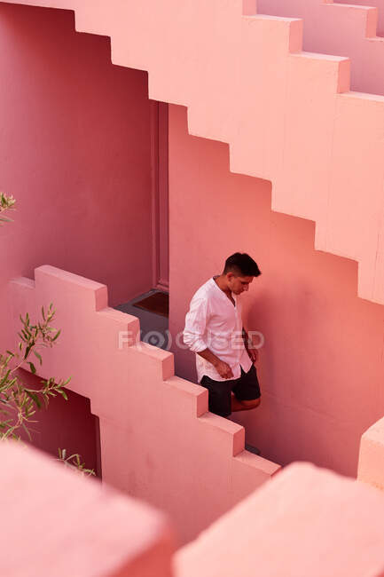 Jeune homme latino descend les escaliers d'un immeuble rose — Photo de stock