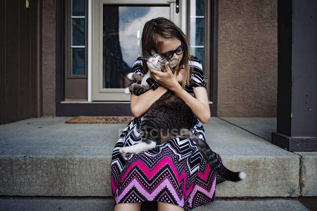 Un pre giovanissima ragazza coccole suo gatto su il anteriore portico di suo casa — Foto stock