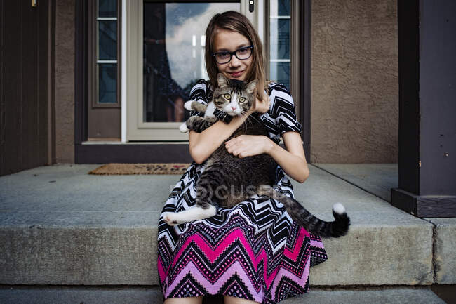 Una ragazza pre adolescente che tiene il suo gatto grigio sul portico anteriore — Foto stock