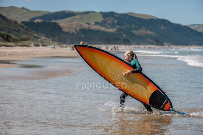 Tween girl carrying a surfboard in New Zealand — Stock Photo