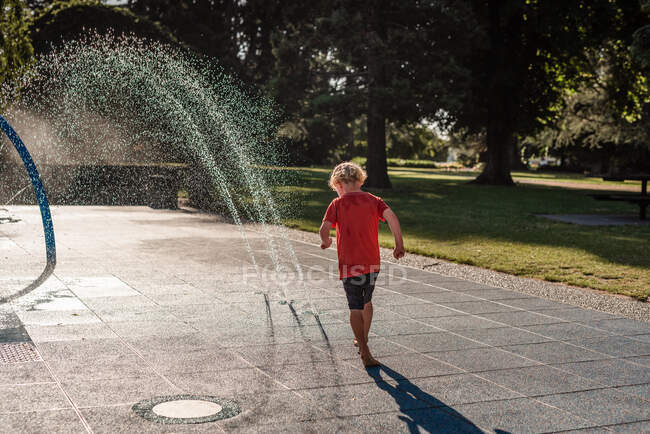 Niño jugando en un parque de salpicaduras en un día de verano - foto de stock