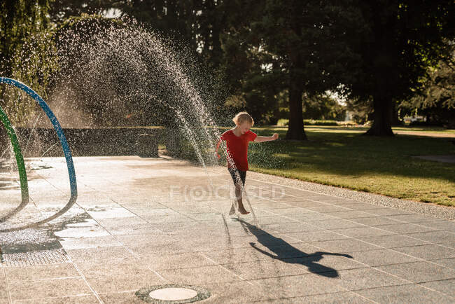 Niño feliz jugando en el agua en un parque - foto de stock