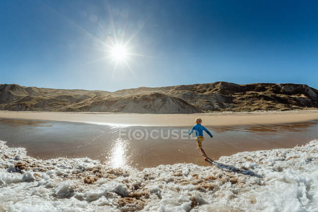 View from ocean of young child running from waves on a sunny day in New Zealand — Stock Photo