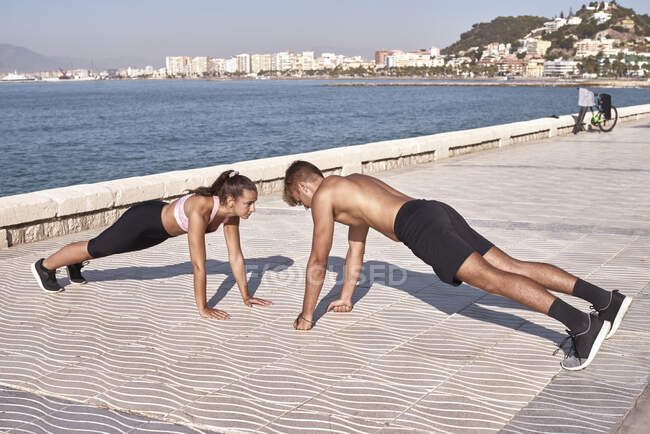 Joven atleta hombre y mujer hacer flexiones en un parque público - foto de stock