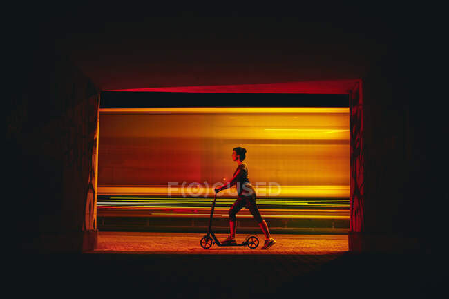 Woman on push scooter at night in the city near the road. — Stock Photo
