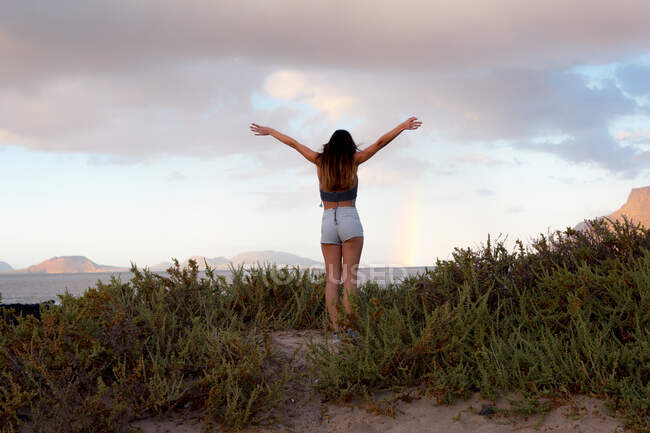 Беззаботная женщина, стоящая с поднятыми на пляже руками во время суммы — стоковое фото