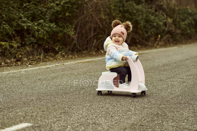 A 12 month old baby driving a toy motorcycle down a road — Stock Photo
