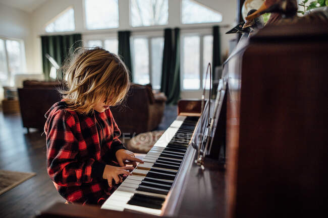 Маленький мальчик с грязными волосами играет на пианино — стоковое фото