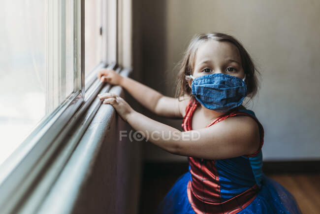 Menina em idade pré-escolar por janela no traje de Halloween e máscara facial — Fotografia de Stock
