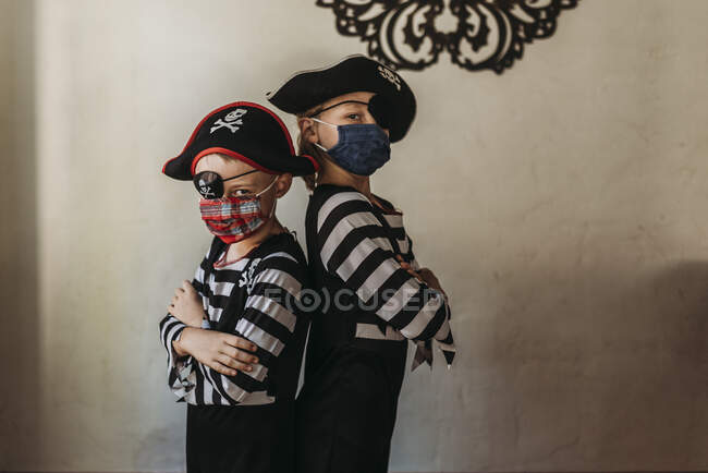 Irmãos em idade escolar vestidos como piratas com máscaras faciais em casa — Fotografia de Stock