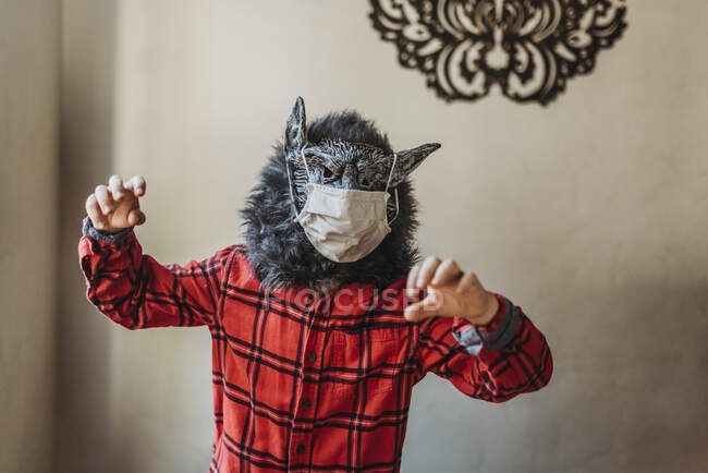Giovane ragazzo in maschera di lupo con la copertura del viso sopra la maschera in piedi a casa — Foto stock