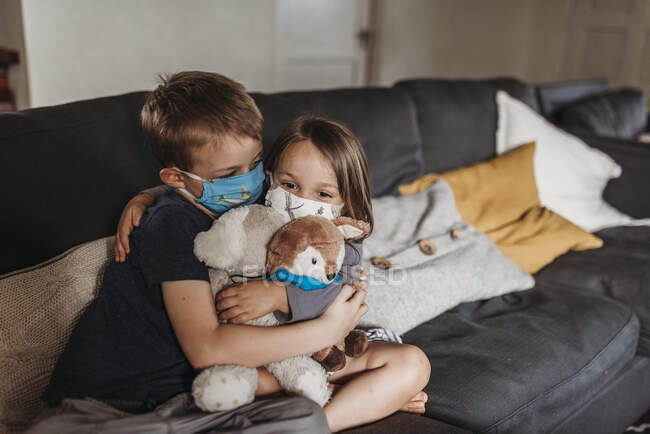 Junge Mädchen und Junge im Schulalter mit Masken, die sich auf der Couch umarmen und lächeln — Stockfoto