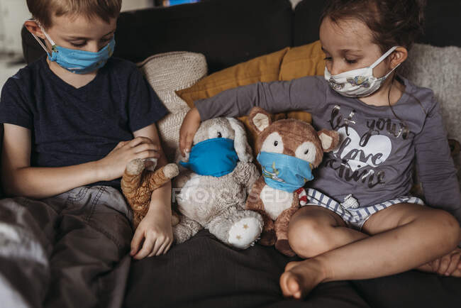 Young girl and young boy with masks playing with animals on couch — Stock Photo