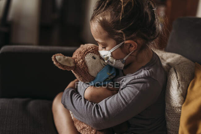 Enfant fille d'âge préscolaire avec masque sur câlin peluche animal avec masque — Photo de stock