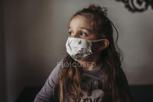 Close up of young girl with mask on looking out window — Stock Photo