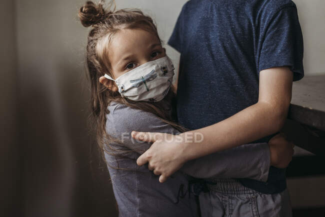 Primer plano de chica joven con máscara en ser abrazado por el hermano mayor - foto de stock