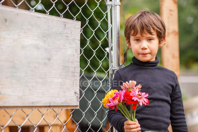 Ein süßer kleiner Junge steht mit einem Strauß Wildblumen vor dem Zaun — Stockfoto