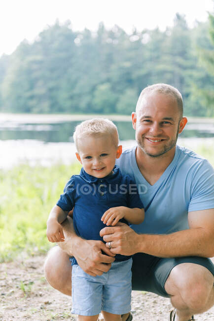 Um jovem pai abraçando seu filho de dois anos de idade, enquanto ambos estão sorrindo — Fotografia de Stock