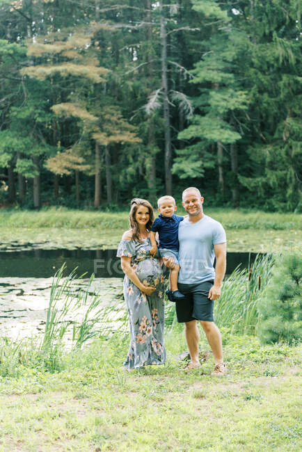 Счастливая растущая семья, стоящая у пруда — стоковое фото