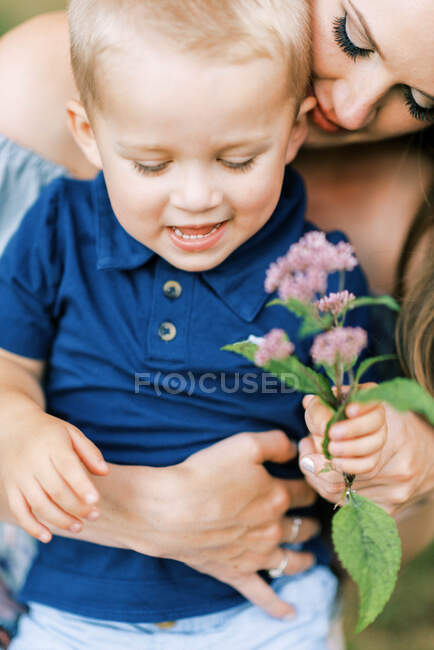 Una madre y su hijo abrazándose amorosamente y jugando con una flor - foto de stock